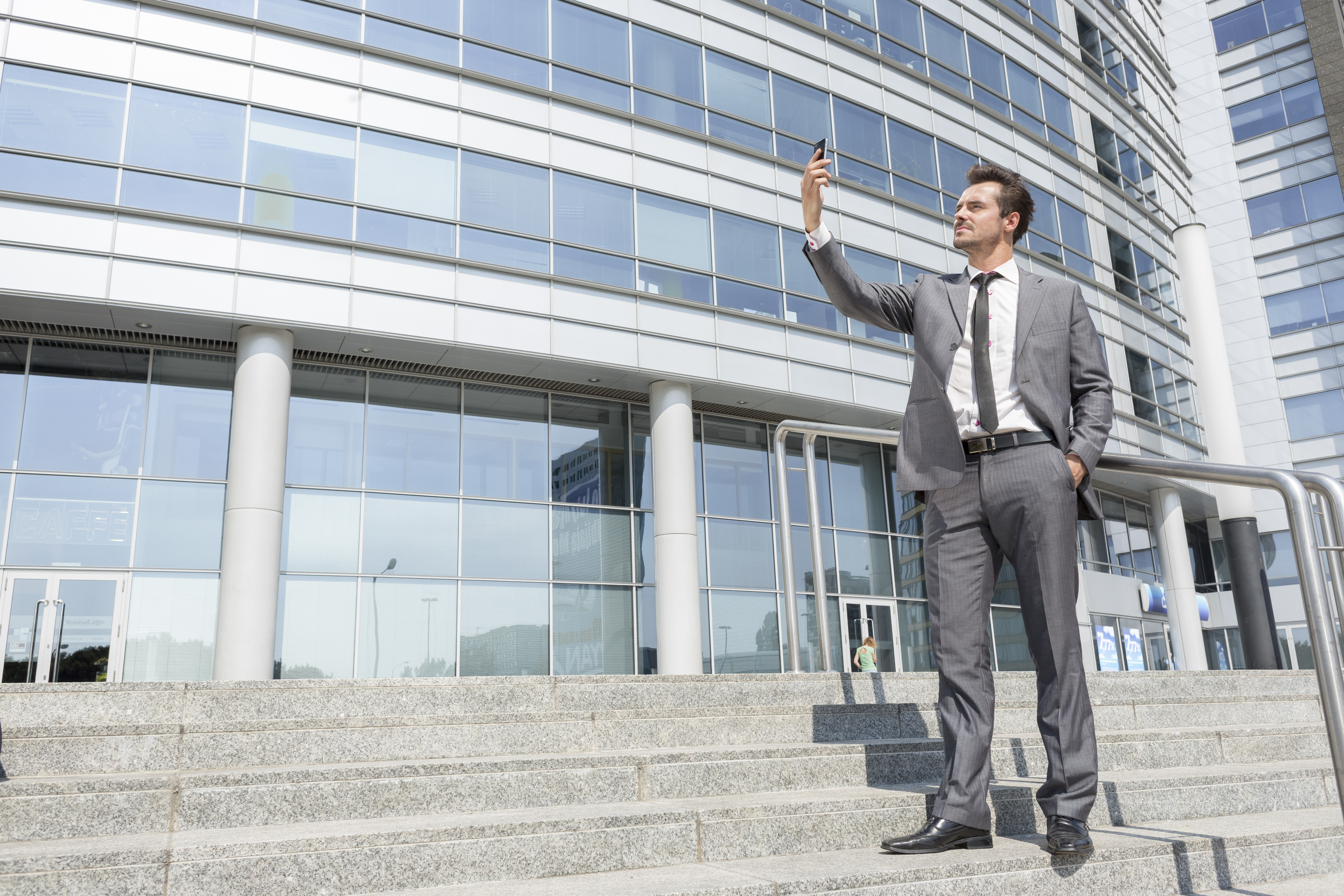 Full length of businessman taking self portrait on steps outside office